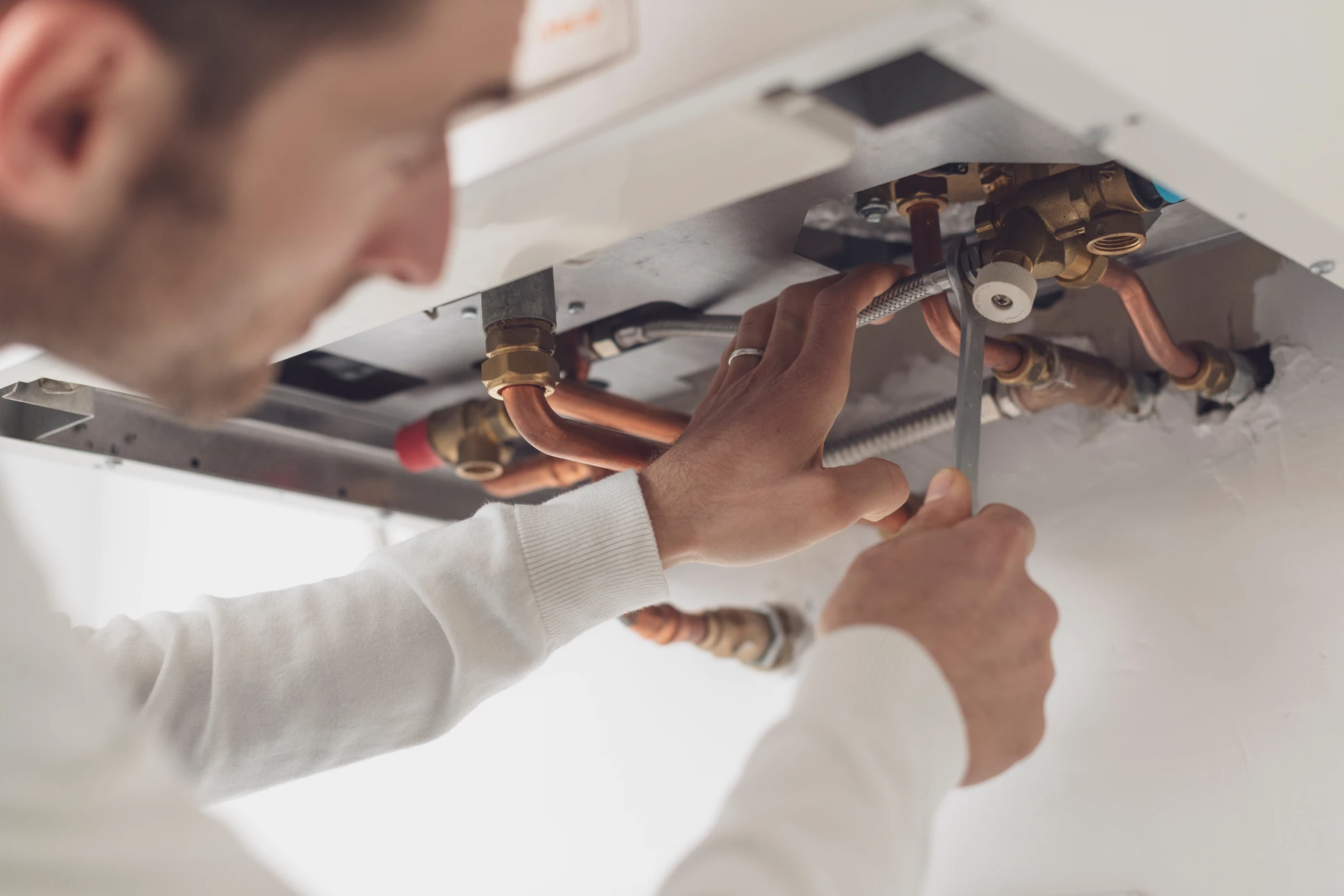 Technicien qualifié en tenue professionnelle effectuant l'installation ou la maintenance d'une unité intérieure de climatisation (console murale ou cassette) dans un salon résidentiel moderne, mettant en évidence le travail de précision et la qualité technique de l'intervention sur cet équipement spécifique.